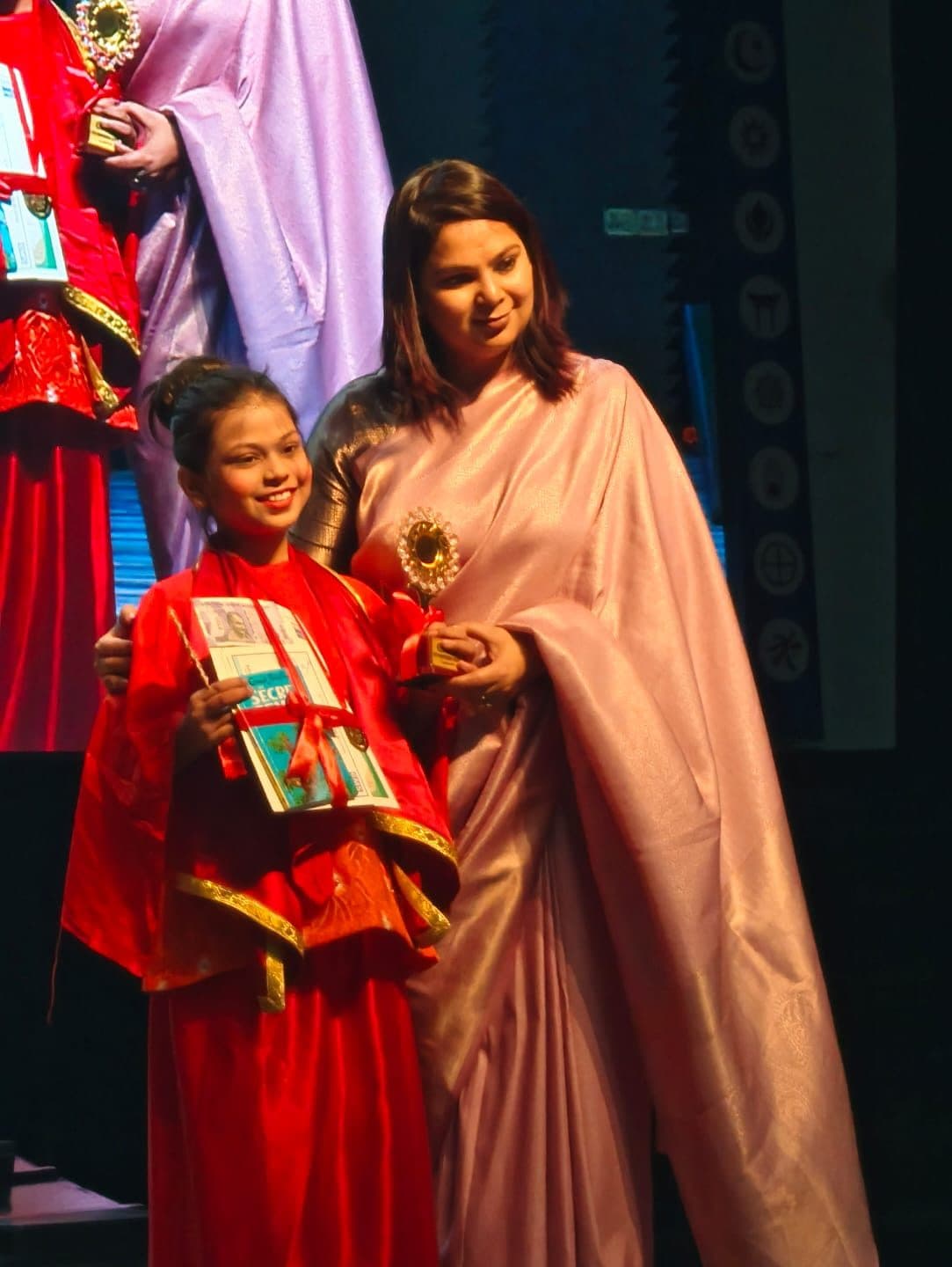 Student receiving an award on stage alongside her teacher