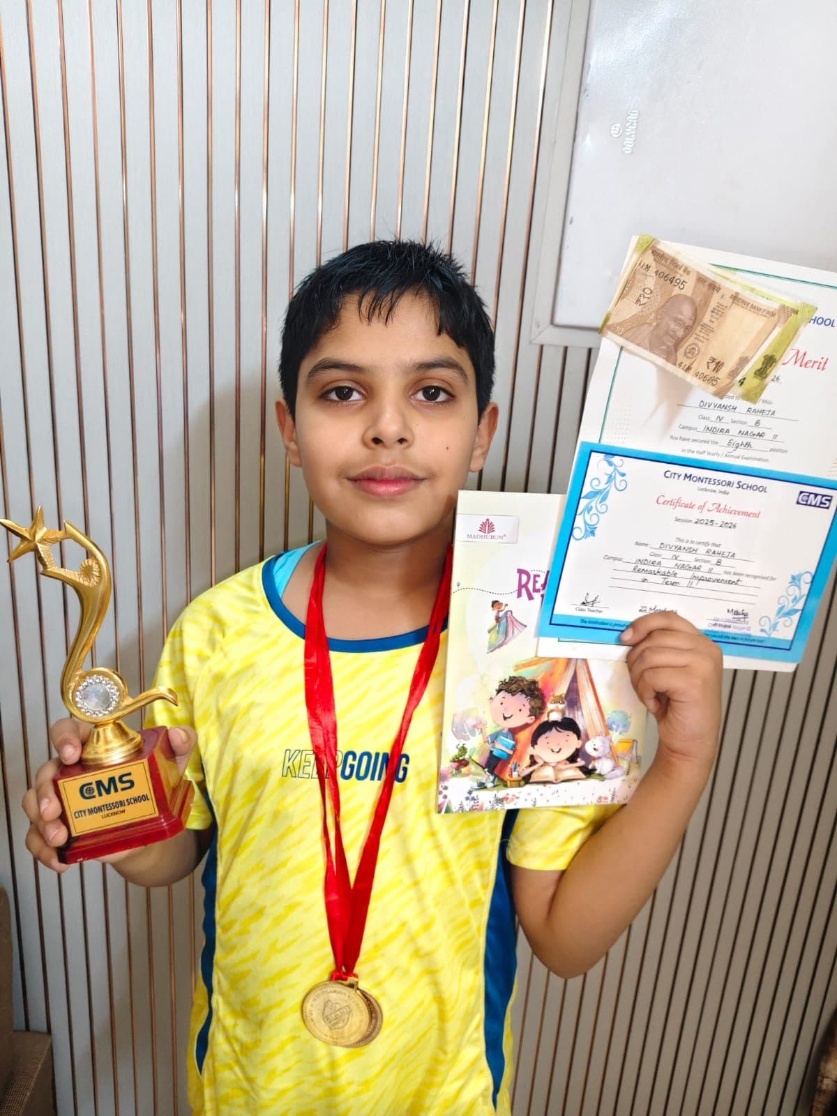 Student holding a trophy, gold medal and certificate of achievement