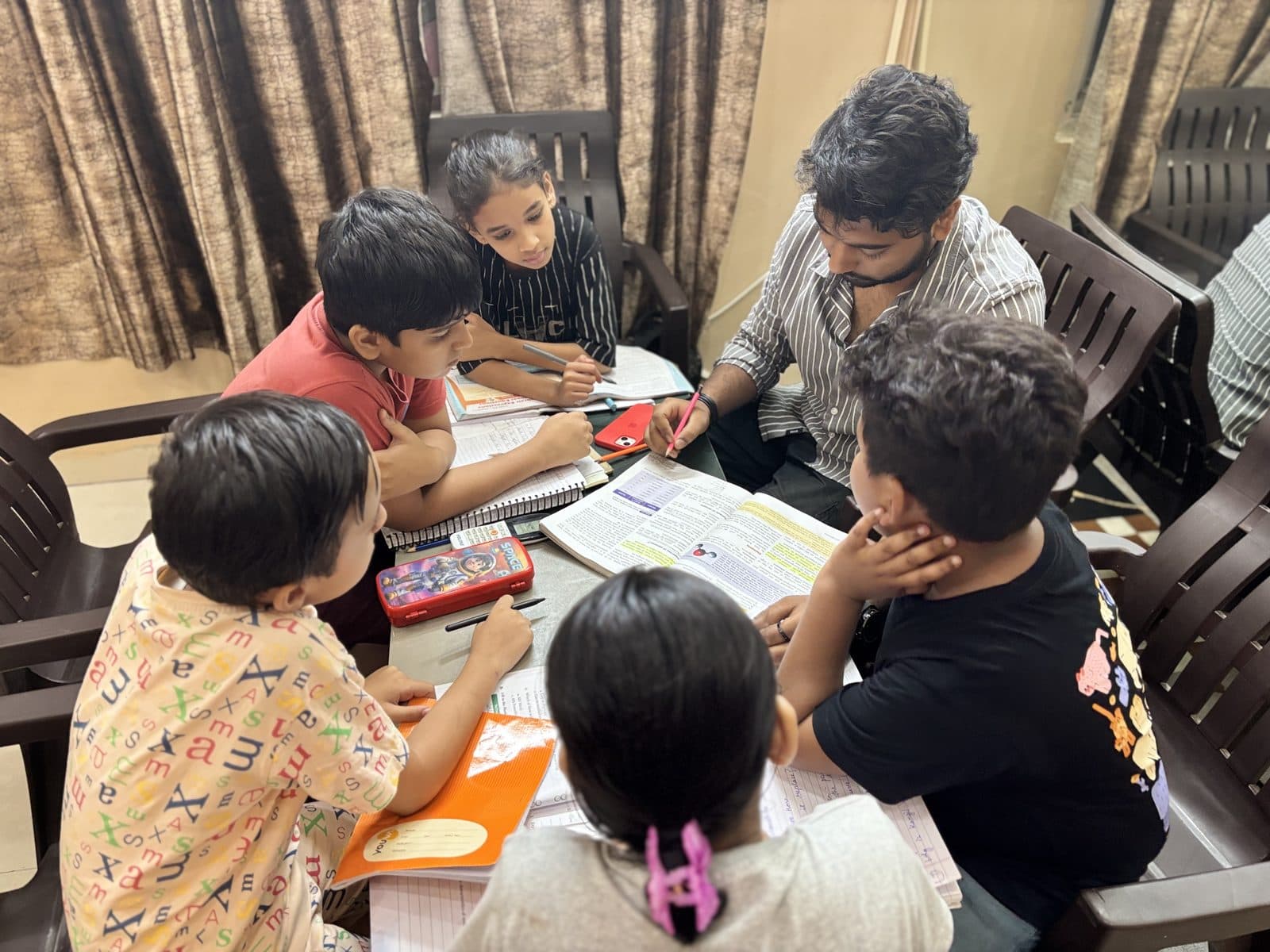 Faculty member teaching a junior batch around a shared study table